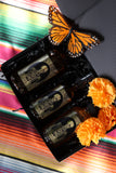 Ancestor Alchemy Kit in a black box with three amber bottles, orange marigolds, and a monarch butterfly decoration.