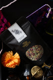 Ancestors loose-leaf tea pouch beside an orange marigold and gold mesh tea infuser in a black gift box.